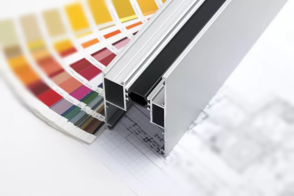 Przekrój aluminiowego profilu ramy z czarną uszczelką, sfotografowany na tle rysunku technicznego i wachlarza próbek kolorów.