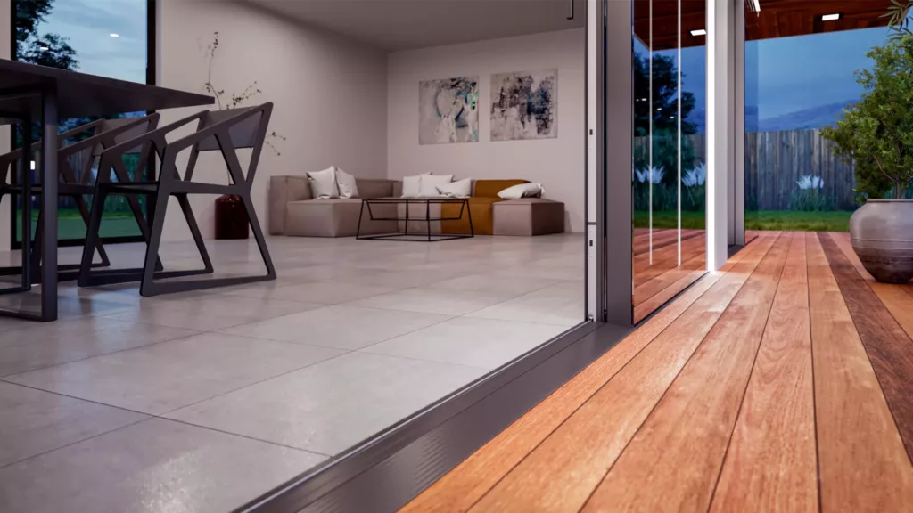 Modern living room with large HST aluminum sliding doors to a terrace with wooden flooring, threshold-free passage, minimalist furniture and a garden in the background.