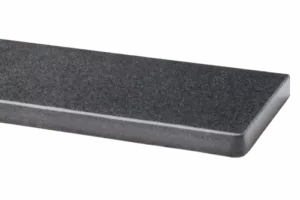 Zbliżenie narożnika ciemnoszarego, teksturowanego parapetu granitowego z delikatnie fazowaną i zaokrągloną krawędzią na jednolitym szarym tle.