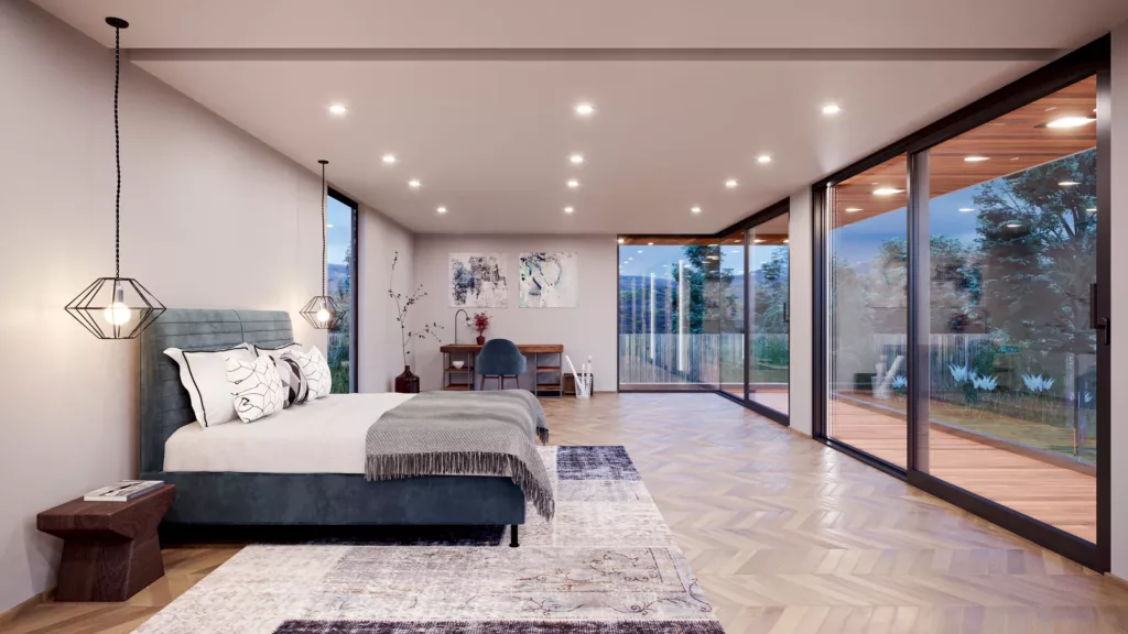 Przestronna, nowoczesna sypialnia z łóżkiem przy wiszących lampach, parkietem w jodełkę i dużymi przeszklonymi drzwiami przesuwnymi HST na taras z widokiem na ogród; w głębi biurko i obrazy na ścianie.