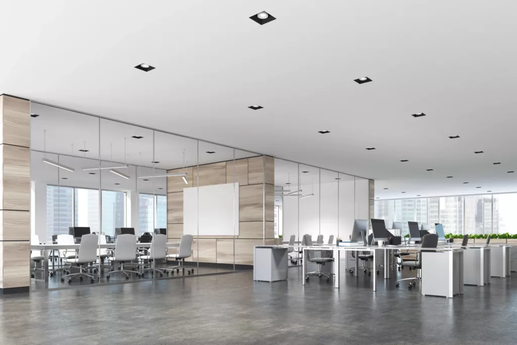 Nowoczesne biuro typu open space z przeszkloną salą konferencyjną, białymi biurkami z komputerami, krzesłami na kółkach i dużymi oknami z widokiem na miasto.