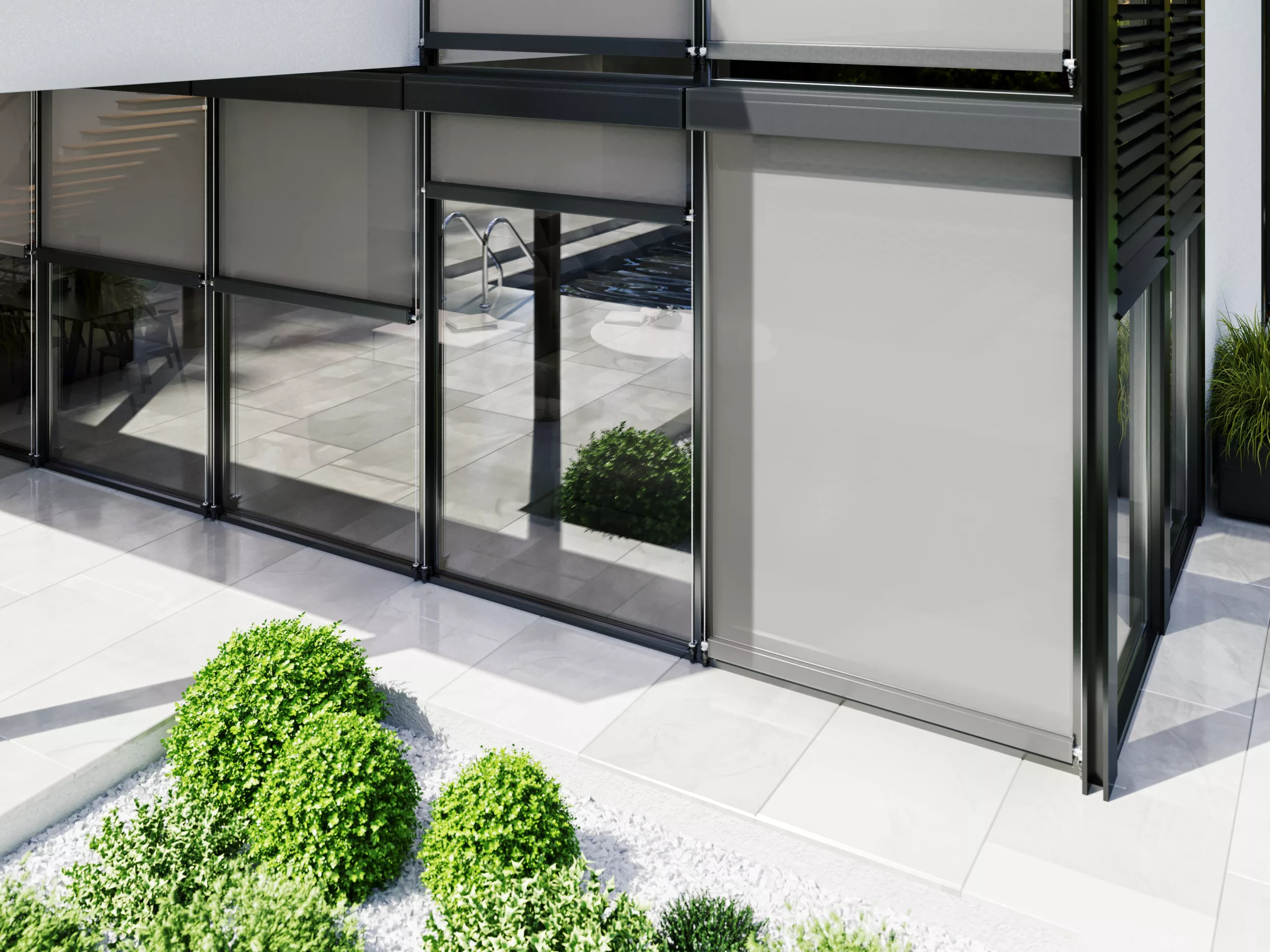 Nowoczesna zabudowa tarasu z aluminiowymi ramami i szklanymi panelami, z opuszczoną roletą screen po prawej, na tle jasnych płyt i formowanej zieleni; w odbiciach widoczny basen.