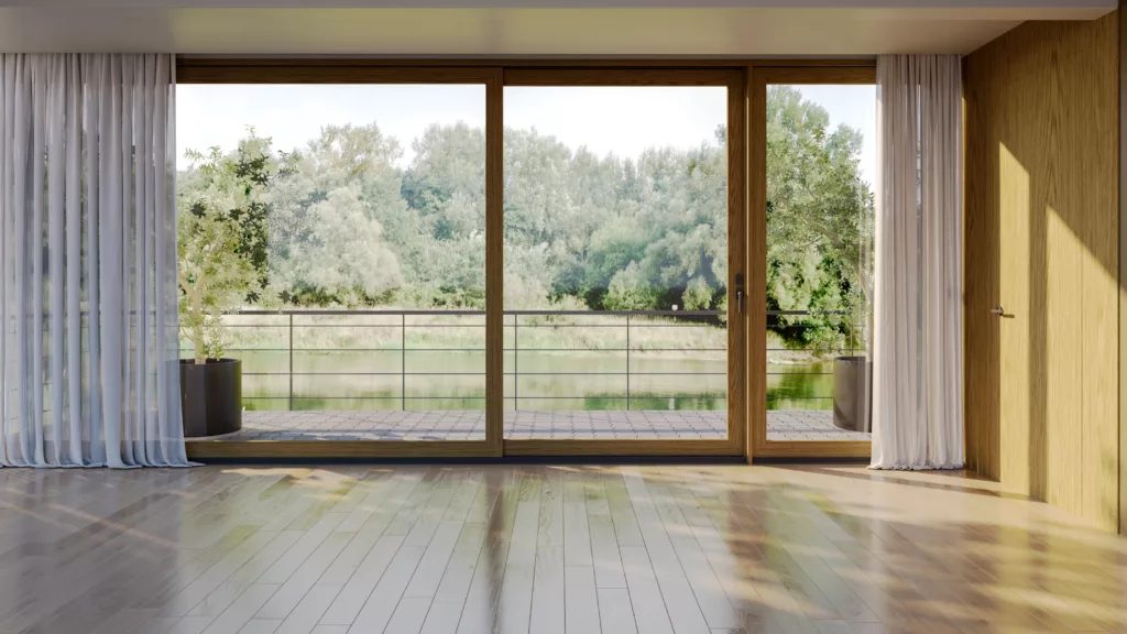 Słoneczny, pusty pokój z drewnianą podłogą i dużymi przeszklonymi drzwiami przesuwnymi prowadzącymi na taras nad wodą, z widokiem na drzewa, białymi zasłonami po bokach i donicami na zewnątrz.