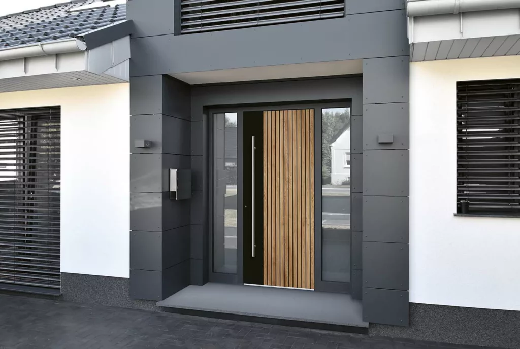 Nowoczesne drzwi zewnętrzne z czarną ramą i pionowym panelem z drewnianych lameli, z długim stalowym pochwytem oraz wąskimi przeszkleniami bocznymi po obu stronach, osadzone w szarej elewacji domu.