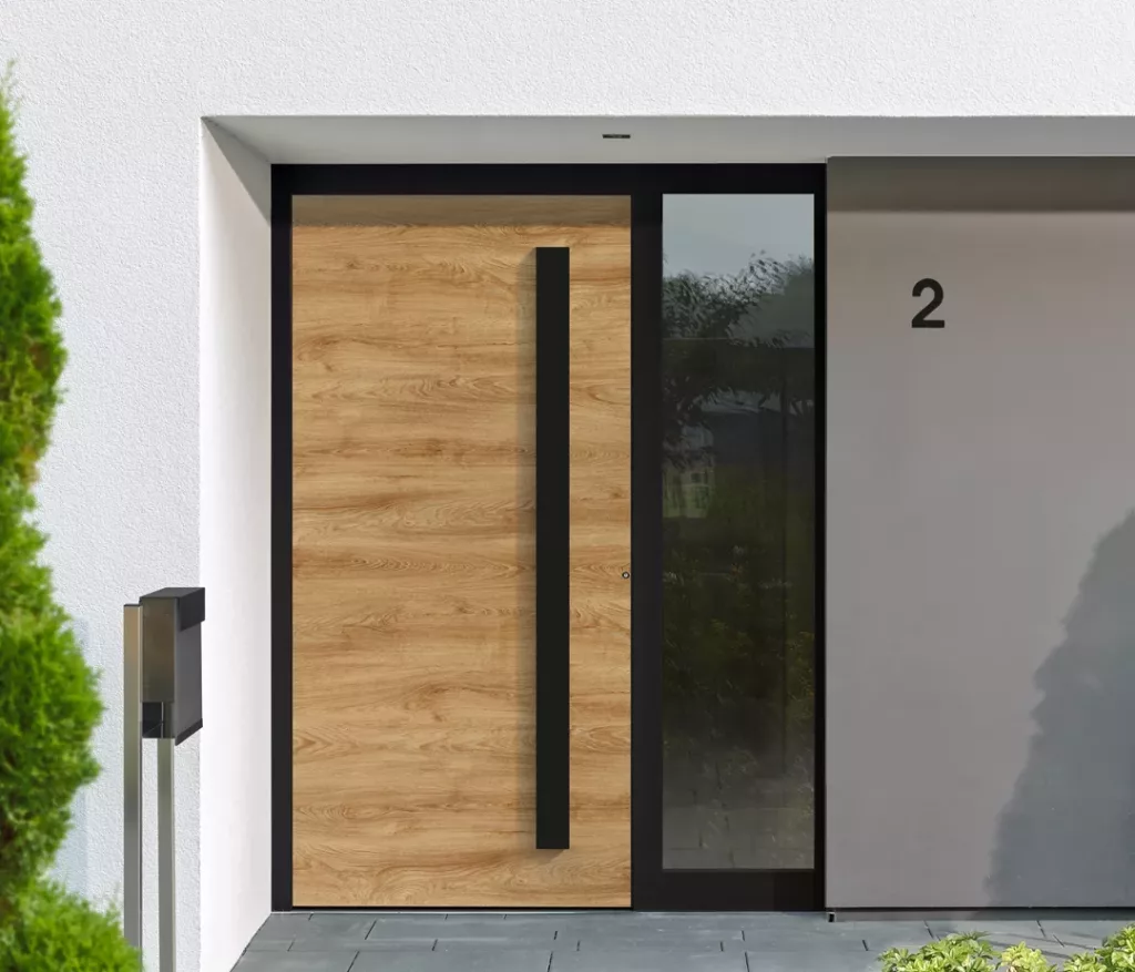 Nowoczesne drzwi zewnętrzne z okleiną drewnianą i czarną pionową klamką, z wąskim naświetlem bocznym w czarnej ramie, w minimalistycznej elewacji w bieli i szarości z numerem 2.
