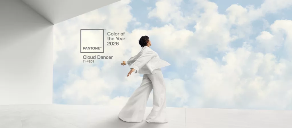 Osoba w białym stroju tańczy na tle chmur; obok napis: Pantone Color of the Year 2026 – Cloud Dancer (11-4201).