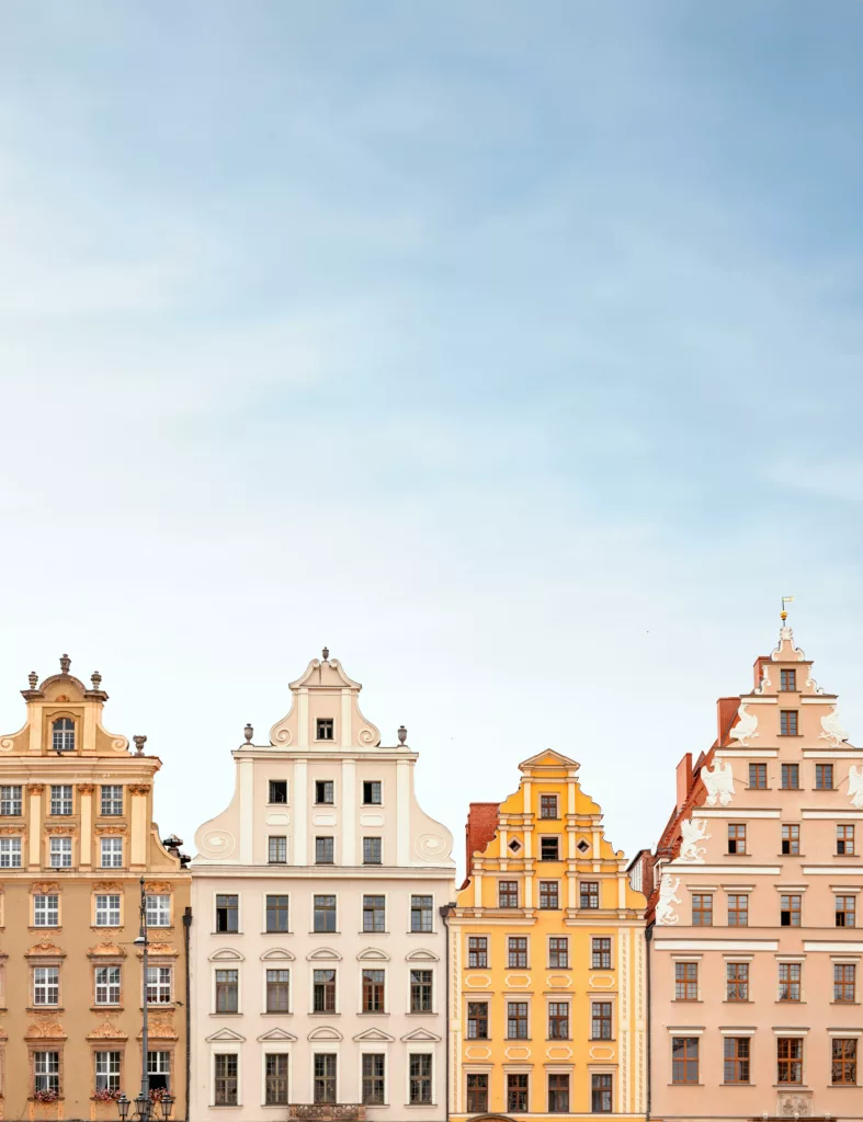 A row of pastel-colored, historic tenement houses with decorative gables and windows against the backdrop of a clear sky.