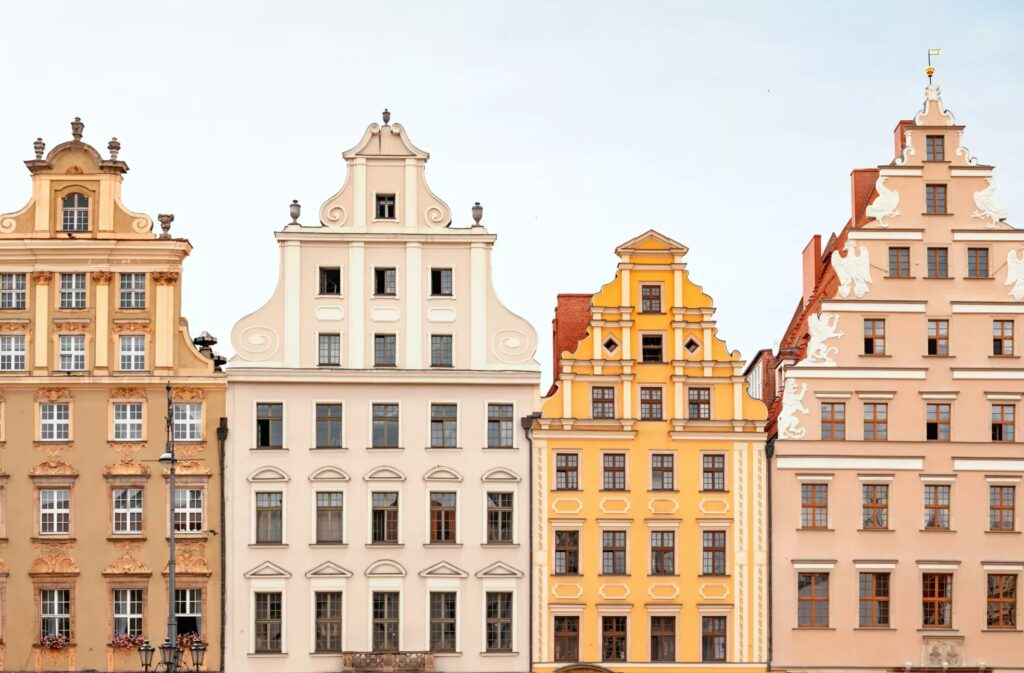 Eine Reihe pastellfarbener, historischer Mietshäuser mit verzierten Giebeln und Fenstern vor dem Hintergrund eines klaren Himmels.